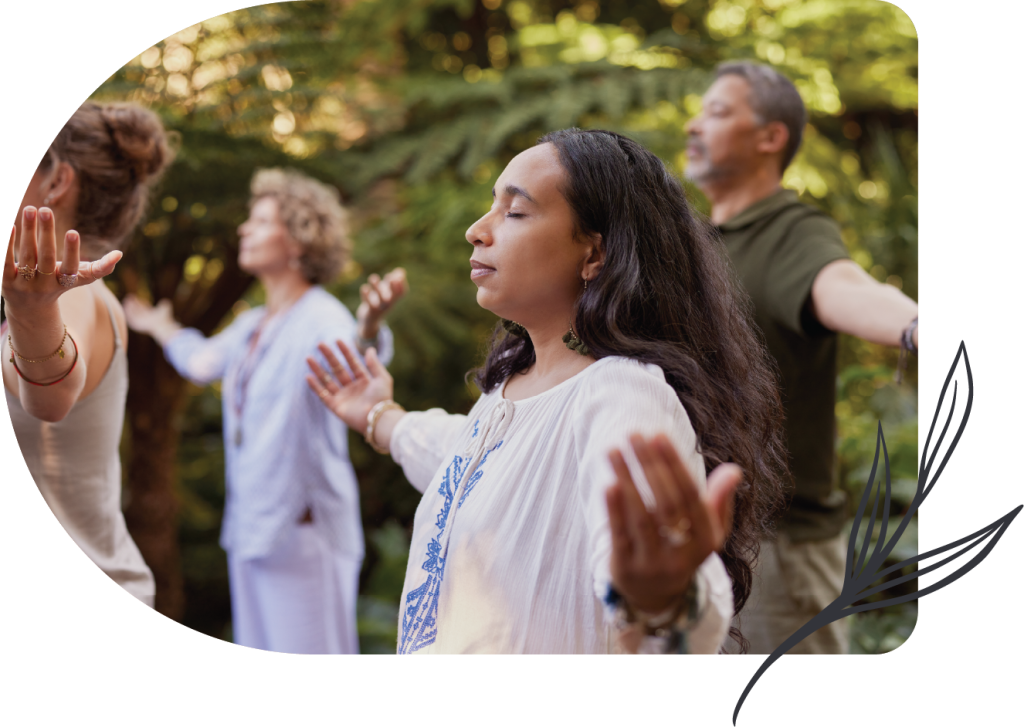 A group of people standing outdoors with eyes closed and arms outstretched, practicing mindfulness or meditation in a natural, green setting as part of the retreat’s additional offerings.